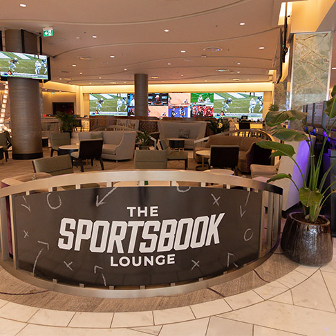 a group of people sitting on a couch watching football on a wall-sized screen